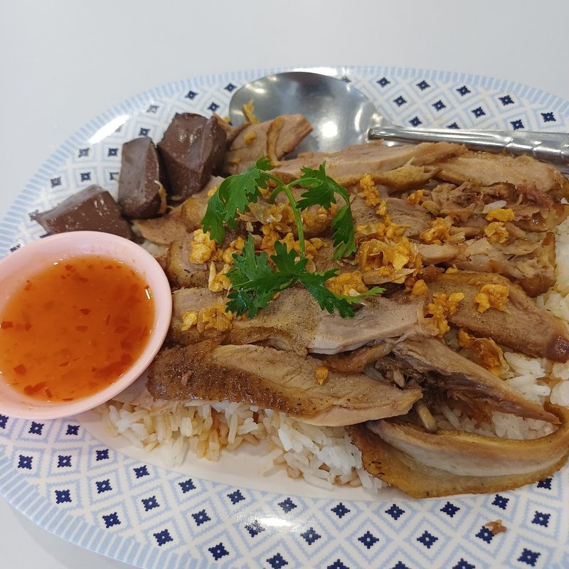 ข้าวหน้าเป็ด เนื้อเป็ดสไลซ์และเลือดเป็ดวางบนข้าวสวย มีกระเทียมเจียว ใบผักชี และน้ำจิ้มรสเผ็ดหนึ่งถ้วย