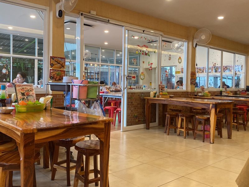 ห้องแอร์ของร้าน โต๊ะไม้และเก้าอี้ไม้ทรงสูง ผนังกระจกมองเห็นด้านนอก