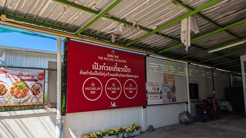 ป้ายไวนิลสีแดง บิบ กูร์มองด์ มิชลินไกด์ ติดผนังร้านใต้หลังคาโรงอาหาร
