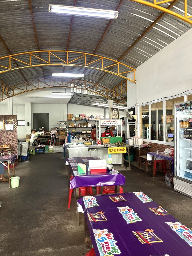โรงอาหารหลังคาสูงข้างร้าน โต๊ะยาวปูผ้าสีม่วง และตู้เครื่องดื่ม